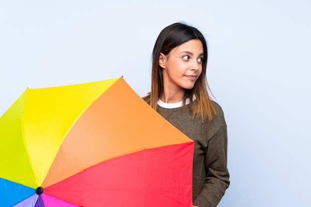 Jovem morena segurando um guarda-chuva sobre parede azul