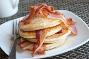 Pancakes layered with slices of bacon, topped with bacon on a white plate