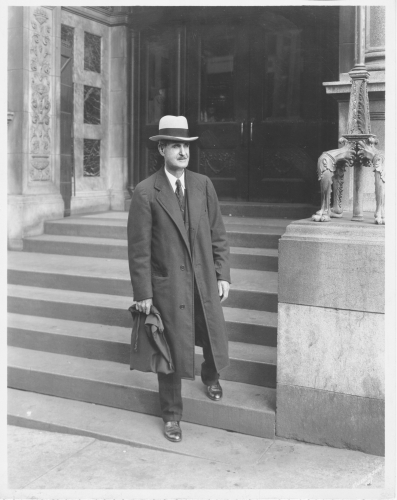 Man with a hat and briefcase standing on the exterior library stairs