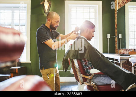 Focused male barber giving customer a haircut in barbershop Stock Photo