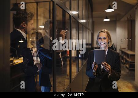 Smiling businesswoman using tablet and two businessmen working on drawing on glass pane in office Stock Photo