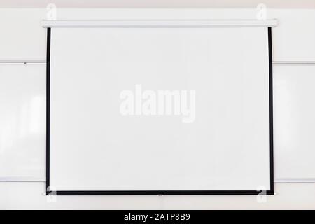 White projection screen over a white board on the classroom wall. Close up with copy space. Stock Photo