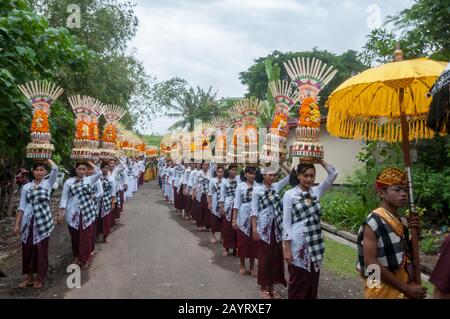 Bali, Indonesia - July 26, 2010: Group of women in traditional costumes and colourful offering on their heads walk to the holy Pura Tanah Lot temple. Stock Photo