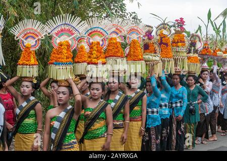 Bali, Indonesia - July 26, 2010: Group of women in traditional costumes and colourful offering on their heads walk to the holy Pura Tanah Lot temple. Stock Photo