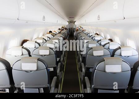 Long aisle with rows of seats and passengers in an airplane cabin (salon) Stock Photo