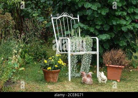 Still life with an old steel garden chair painted white in the garden August Stock Photo