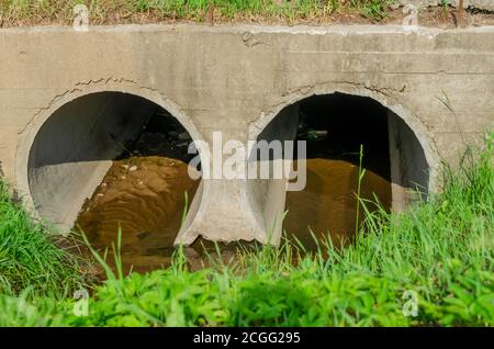 Two round pipes through which a small river flows. These pipes run under the roadway. Stock Photo