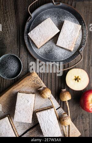 Delicious pie made from leavened dough with poppy seed and apple filling, sprinkled with powdered sugar on rustic wooden background Stock Photo