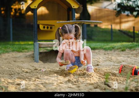 Beautiful baby  having fun on sunny warm summer day - Cute toddler girl playing in sand on outdoor playground Stock Photo