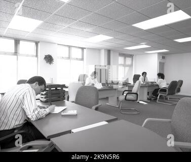 1989, historical, male and female employees working at their desks in a spacious open-plan office, England, UK. Large semi-circular desks with surrounding chairs for informal meetings and personal computers of the era can be seen. Stock Photo