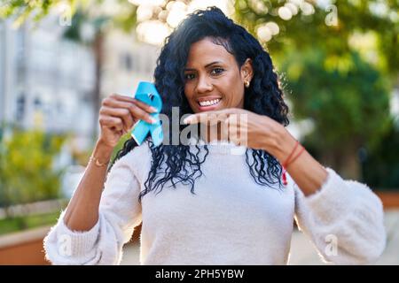 Middle age hispanic woman holding blue ribbon smiling happy pointing with hand and finger Stock Photo