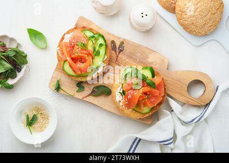 Open smoked salmon sandwiches with cream cheese, cucumber, sesame seeds, microgreens, spinach, and peas leaves on light old wooden background. Healthy Stock Photo