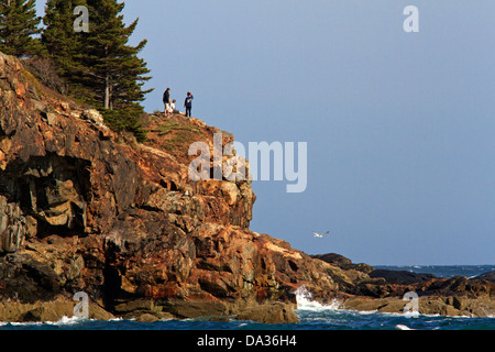 Three people standing on a cliff at Sand Beach, Acadia, National Park, Maine. Stock Photo