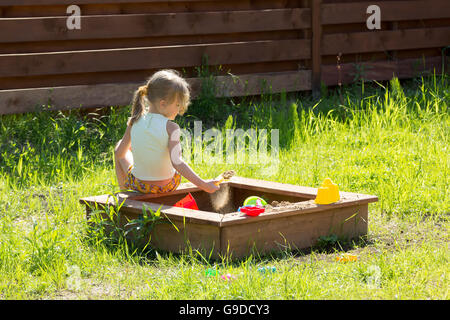 little girl sitting back playing in a sandbox Stock Photo