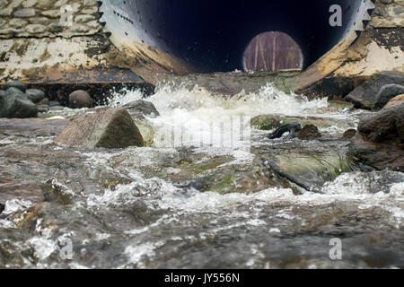 Culvert - drain under road for small river. Big pipe under freeway, highway engineering; roadmaking. At other end of pipe visible wood Stock Photo