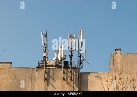 Mobile antenna on the roof of a building against blue sky. Broadcasting and network communicators, receivers. Modern phone and communication tech Stock Photo