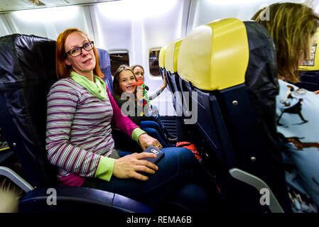 Family sitting on leather seats in commercial aircraft. Mother and daughters are sitting on a low cost airlines passenger jet plane. Stock Photo