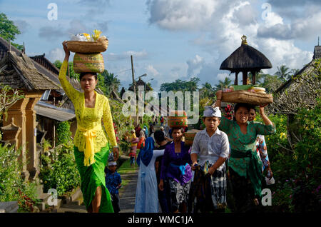 Young Balinese women carrying baskets on their heads in traditional dress in Penglipuran Village, Bali, Indonesia Stock Photo