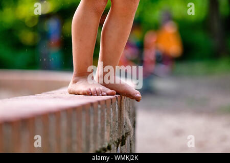 Low section of a caucasian child girl who is standing barefoot on a little stone wall with sandy feet in summer Stock Photo