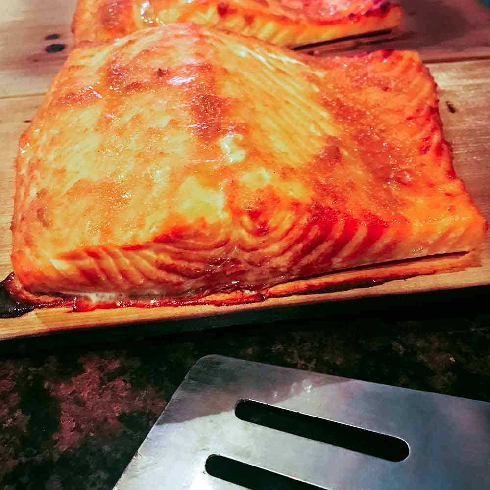 Two golden fillet of cedar plank–grilled salmon on wood