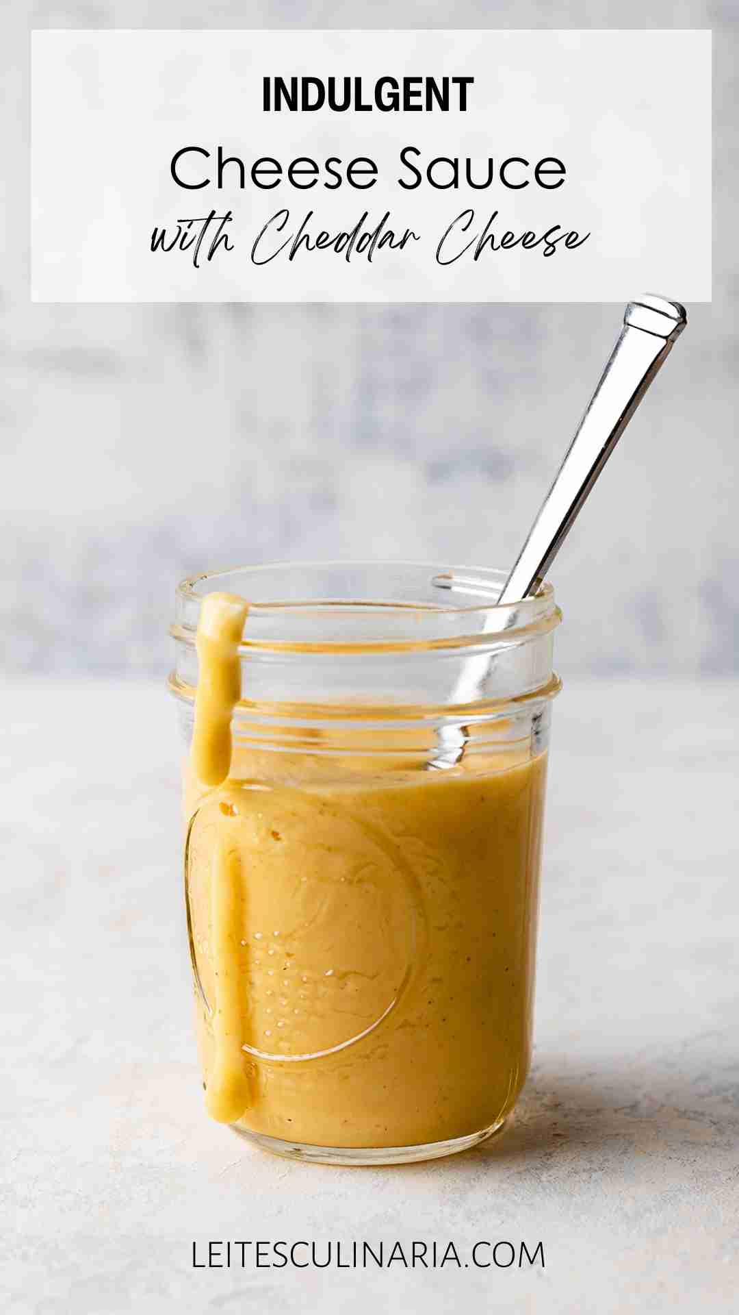 A Mason jar filled with homemade Cheddar cheese sauce with a spoon resting inside and a drip of sauce down the side of the jar.