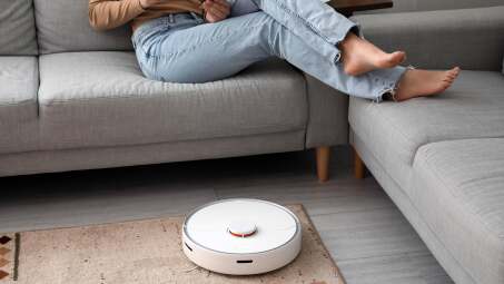 Woman sitting on couch while robot vacuum cleaner vacuums the floor