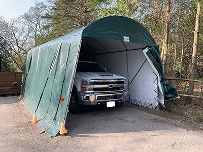 A truck is parked under a tent in a driveway.