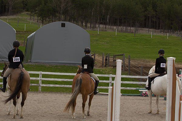 Three people are riding horses in a fenced in area.