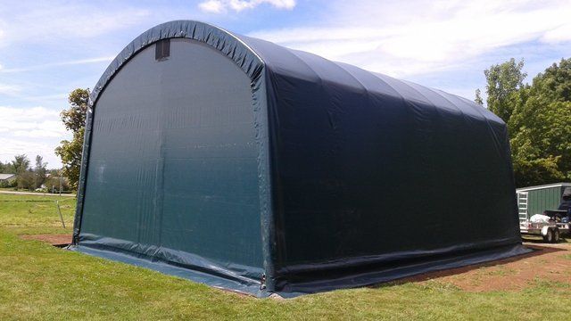 A large green tent is sitting in the middle of a grassy field.