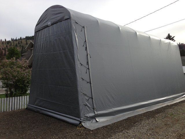 A large gray tent is sitting on top of a gravel driveway.