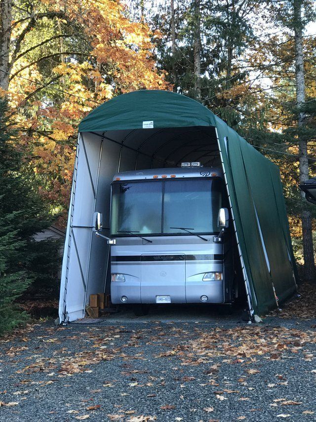 A rv is parked under a green tent in the woods