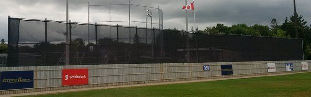 A baseball field with a fence and a canadian flag in the background