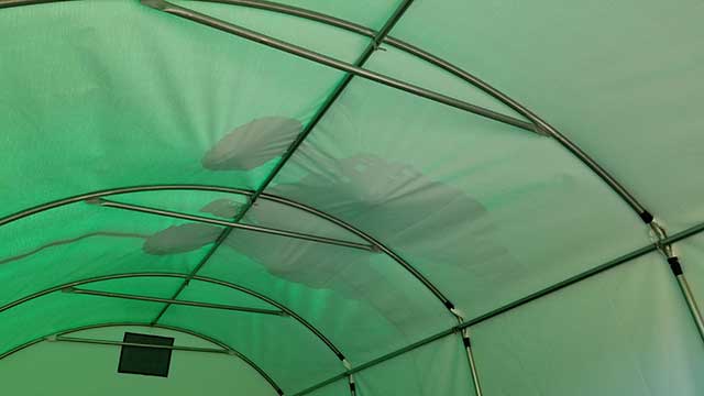 The inside of a greenhouse with a fan hanging from the ceiling.