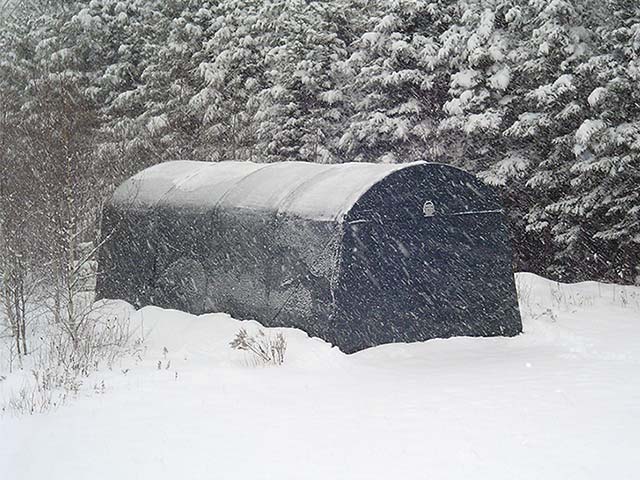 A black tent is sitting in the middle of a snowy forest.