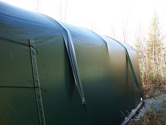 A large green tent is sitting in the middle of a forest.