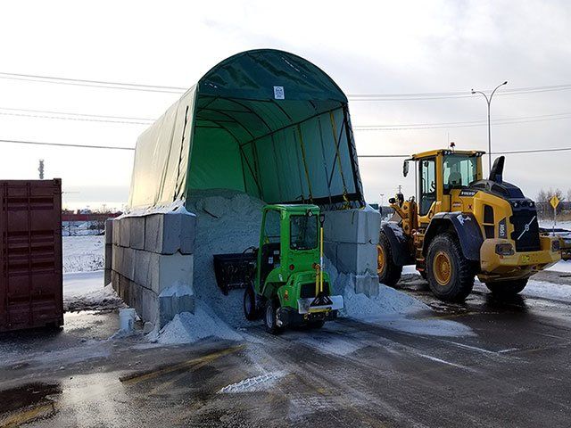 A green forklift is loading salt into a container next to a yellow tractor.