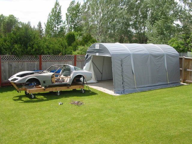 A car is sitting under a tent in a backyard