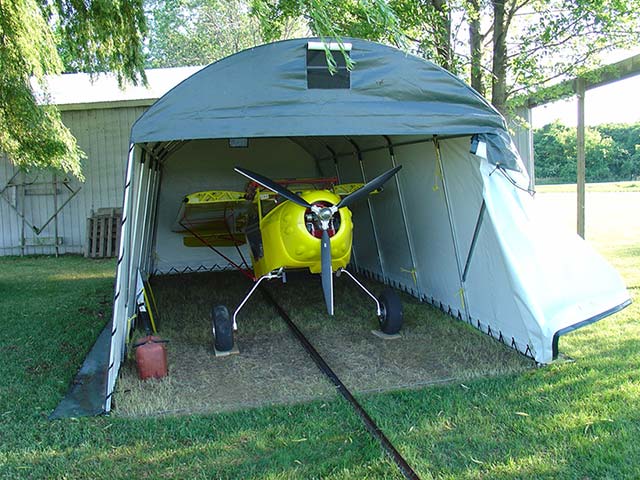 A small yellow airplane is parked under a tent