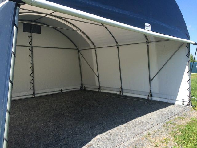 A white tent with a blue roof is sitting on gravel