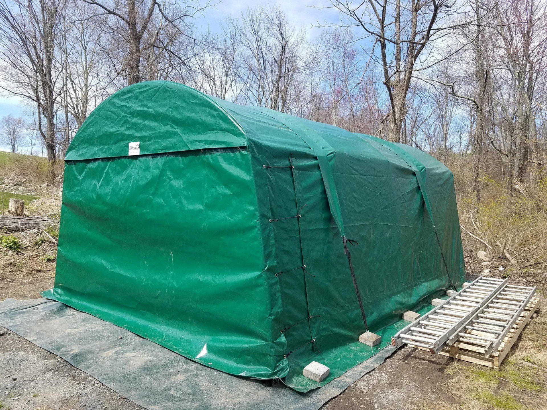 A green tent is sitting on the ground next to a ladder.