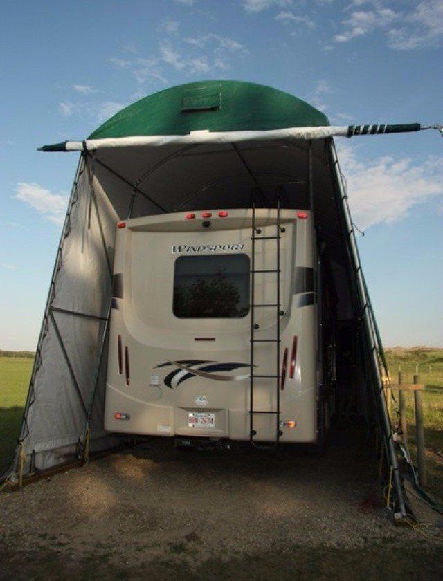 A white rv is parked under a green tarp