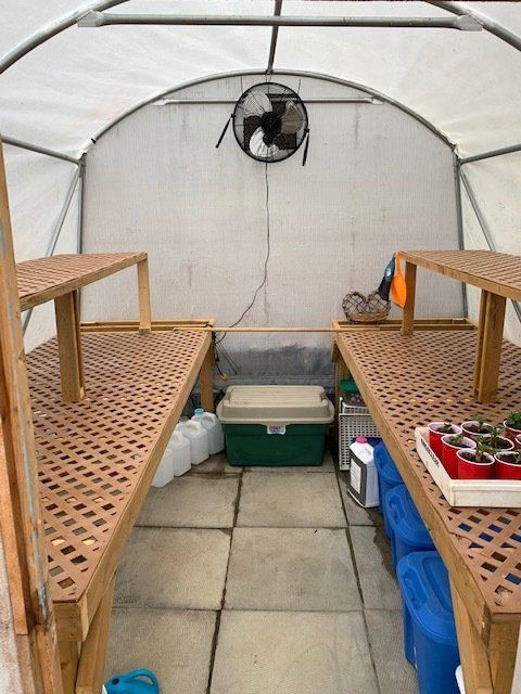 A greenhouse with wooden shelves and a fan