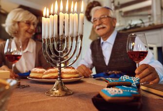 Older couple smiling and drinking wine at dinner table with lit menorah 