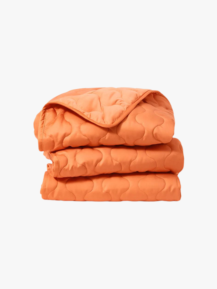 Folded up orange blanket with wavy stitching on it.