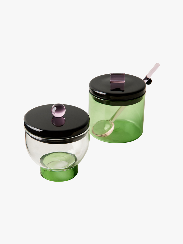 Two green glass bowls with black glass lids and pink knobs.