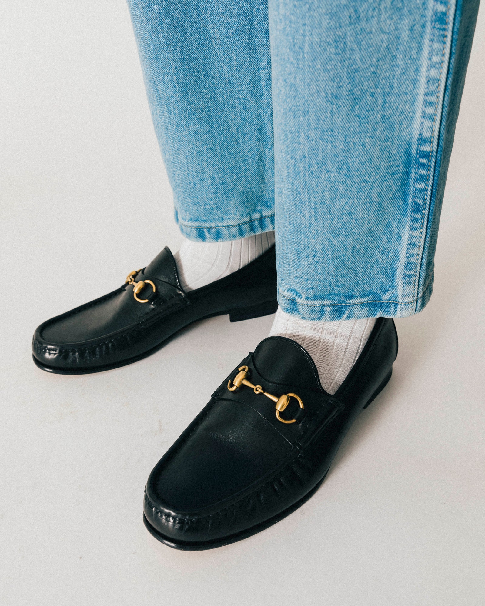 A pair of black Gucci 1953 Horsebit Leather Loafers styled with white socks and blue denim