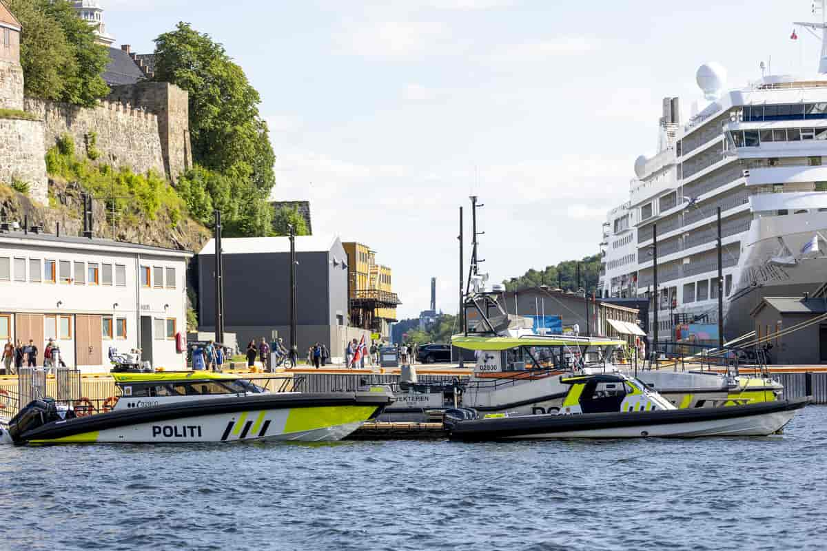 Tre forskjellige politibåter ved en brygge. Til venstre en høy mur. I bakgrunnen et stort cruiseskip.