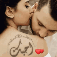 a man is kissing a woman on the back of her neck with a tattoo .