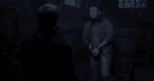 a man is standing next to another man in a dark room with his hands tied .