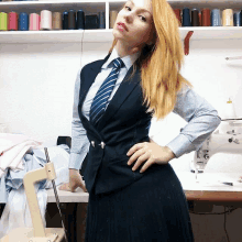 a woman wearing a blue vest and tie stands in front of a sewing machine